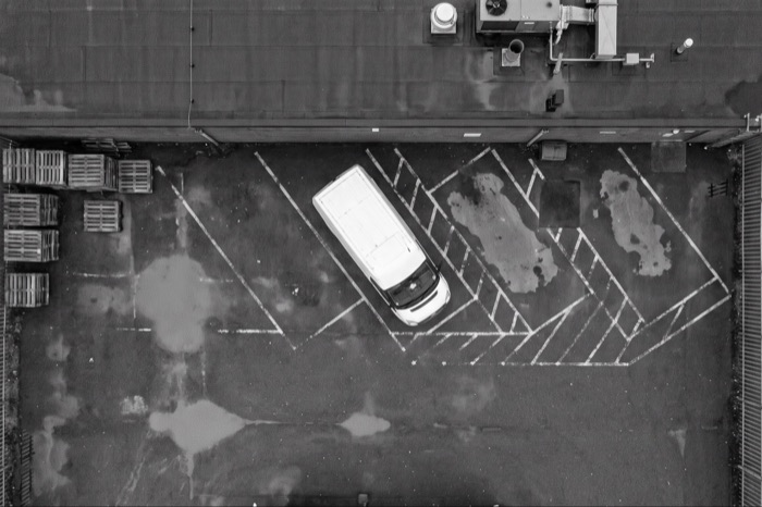 Drone survey photograph looking straight down over an industrial yard with a parked white van, stacked pallets and painted line markings