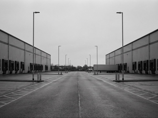Empty service road between two steel-clad distribution warehouses at dusk